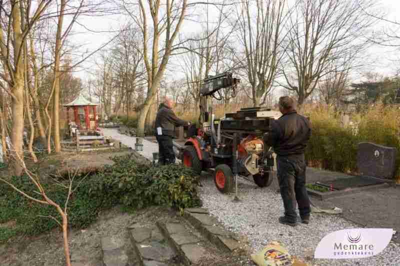 Vaklieden plaatsen een grafmonument met een minikraan op de begraafplaats